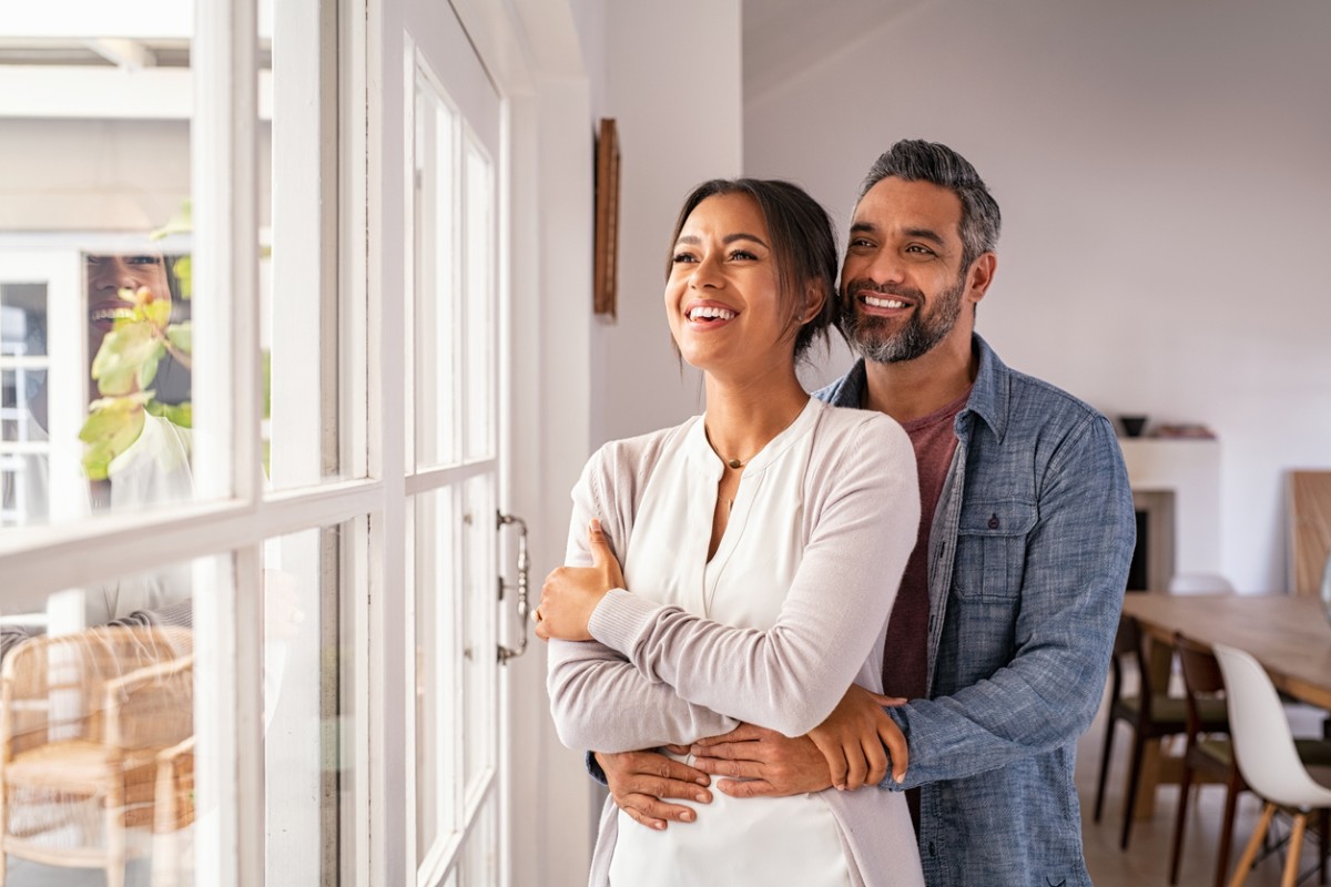 Couple souriant enlacé dans un intérieur lumineux, symbole d’un amour enraciné et complice pour célébrer 5 ans de mariage et les noces de bois.